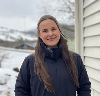 Kvinne, med blå jakke, og hvit bakgrunn.